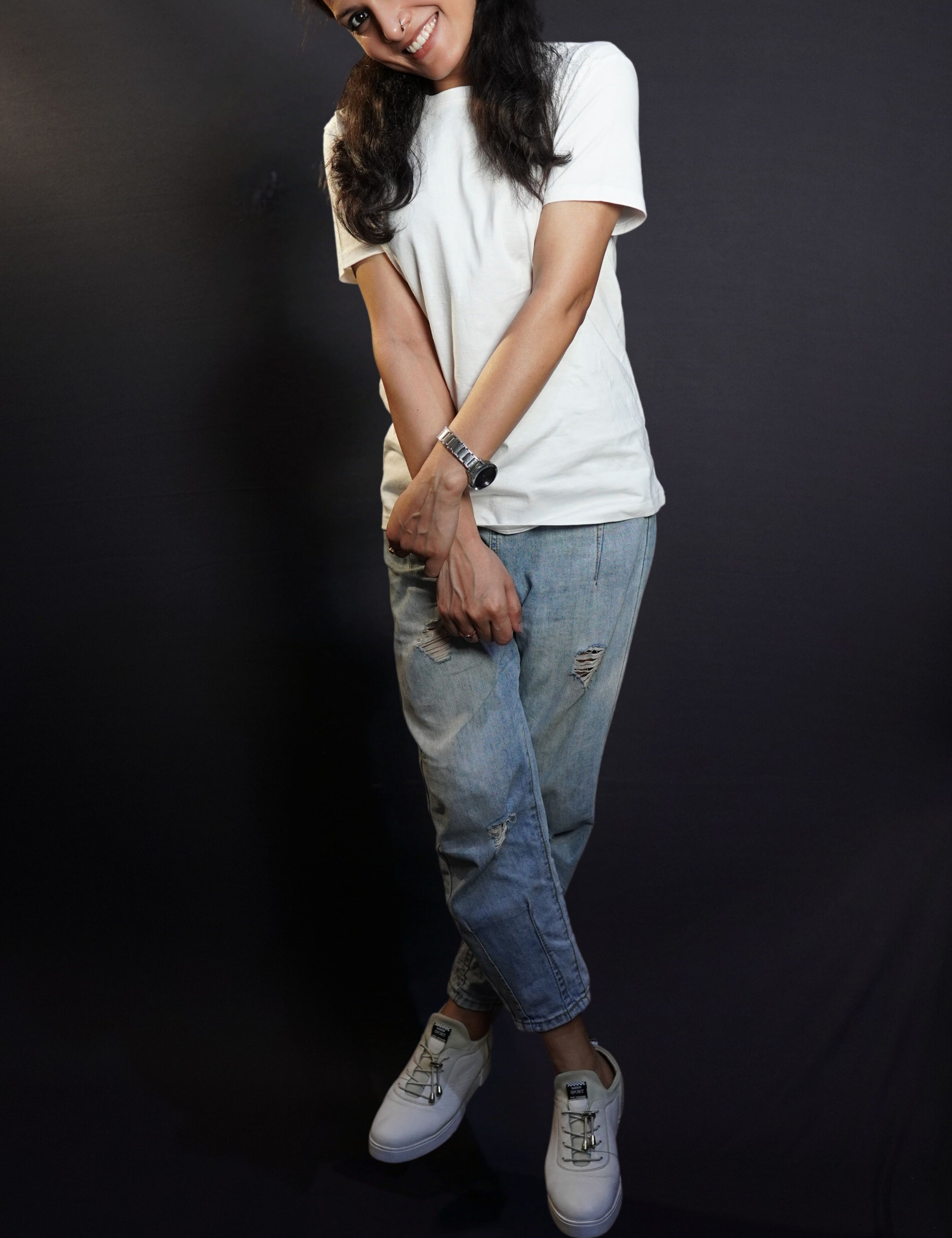 A woman wearing a plain plus size men's snowy white round neck t-shirt, posing with her hand grabbing the wrist of the other, smiling brightly, highlighting a trendy baggy fit-Muselot