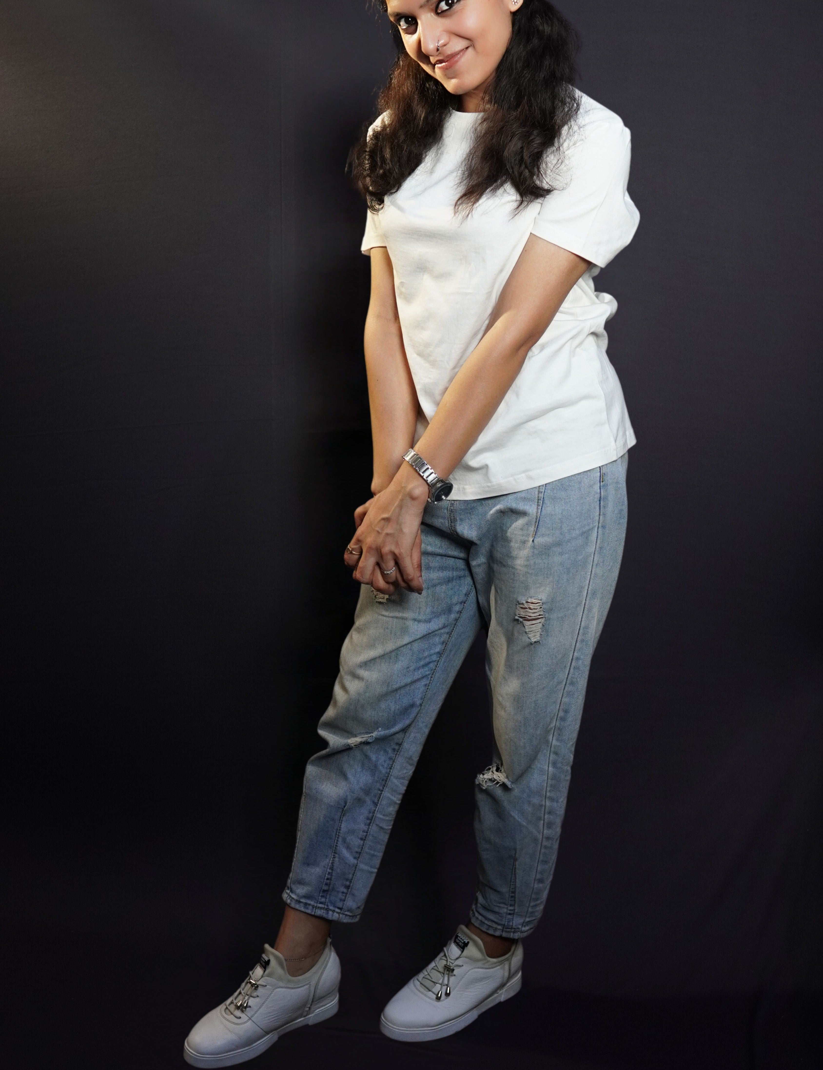 A woman wearing a stretchable long length round neck short sleeved snowy white t-shirt, posing with her hands grabbing each other, stretched, highlighting an easygoing snug fit-Muselot