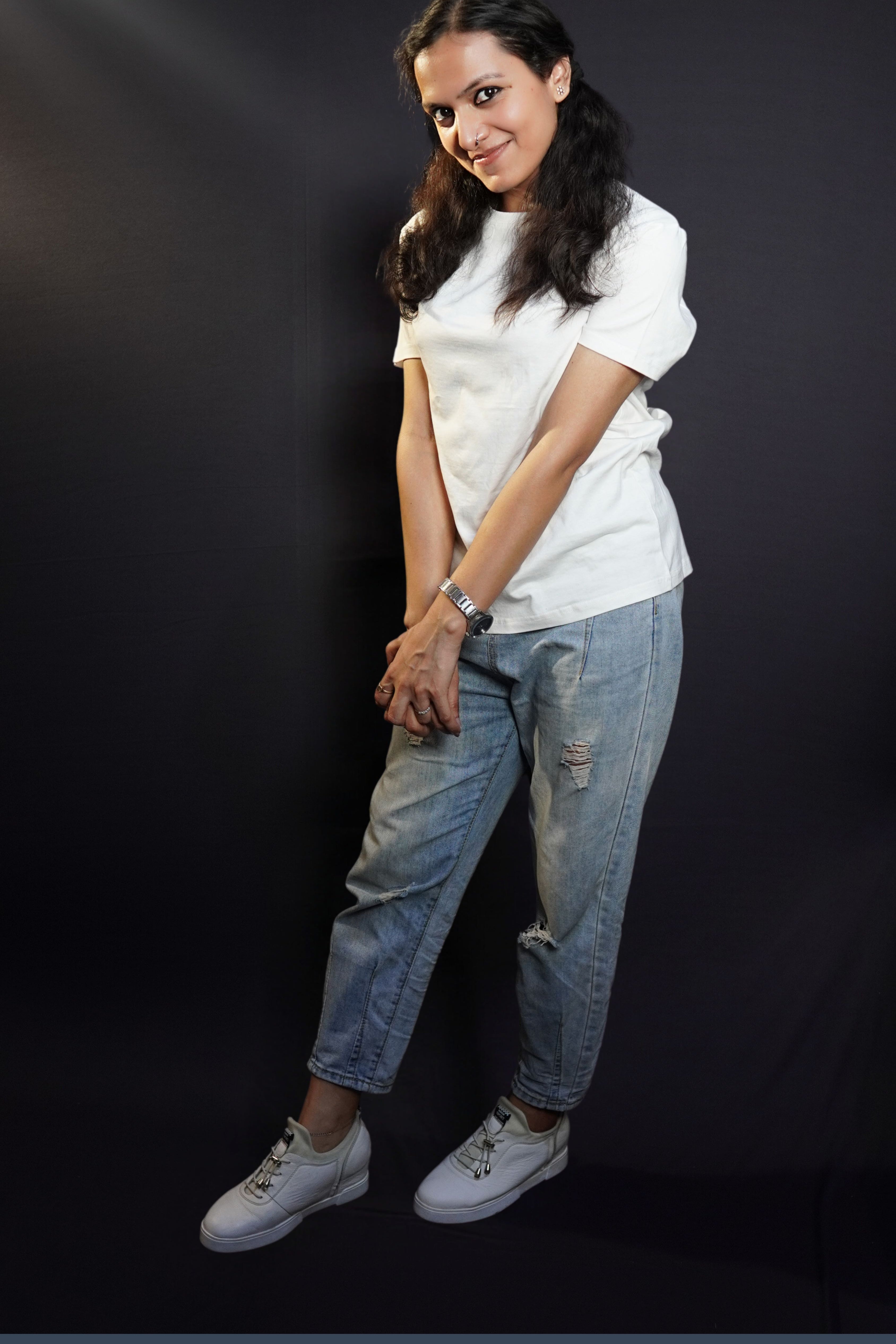 A woman wearing a stretchable long length round neck short sleeved snowy white t-shirt, posing with her hands grabbing each other, stretched, highlighting an easygoing snug fit-Muselot