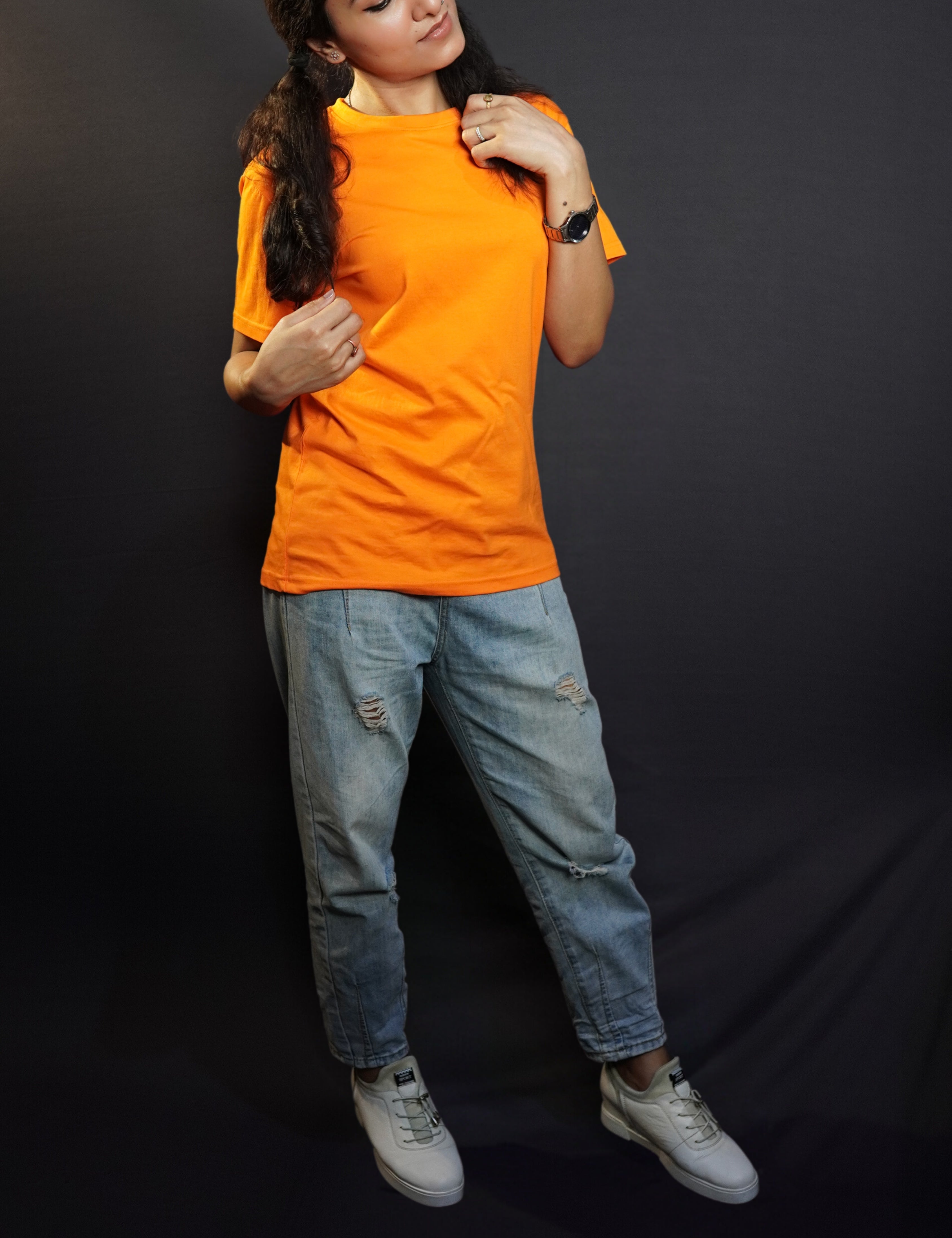 A model in a women's short sleeved summer tropical orange t-shirt, posing with hand grabbing a section of her short her and other just grabbing of the tip of other section on her shoulder, bending her head slightly, showcasing a modern informal look-Muselot