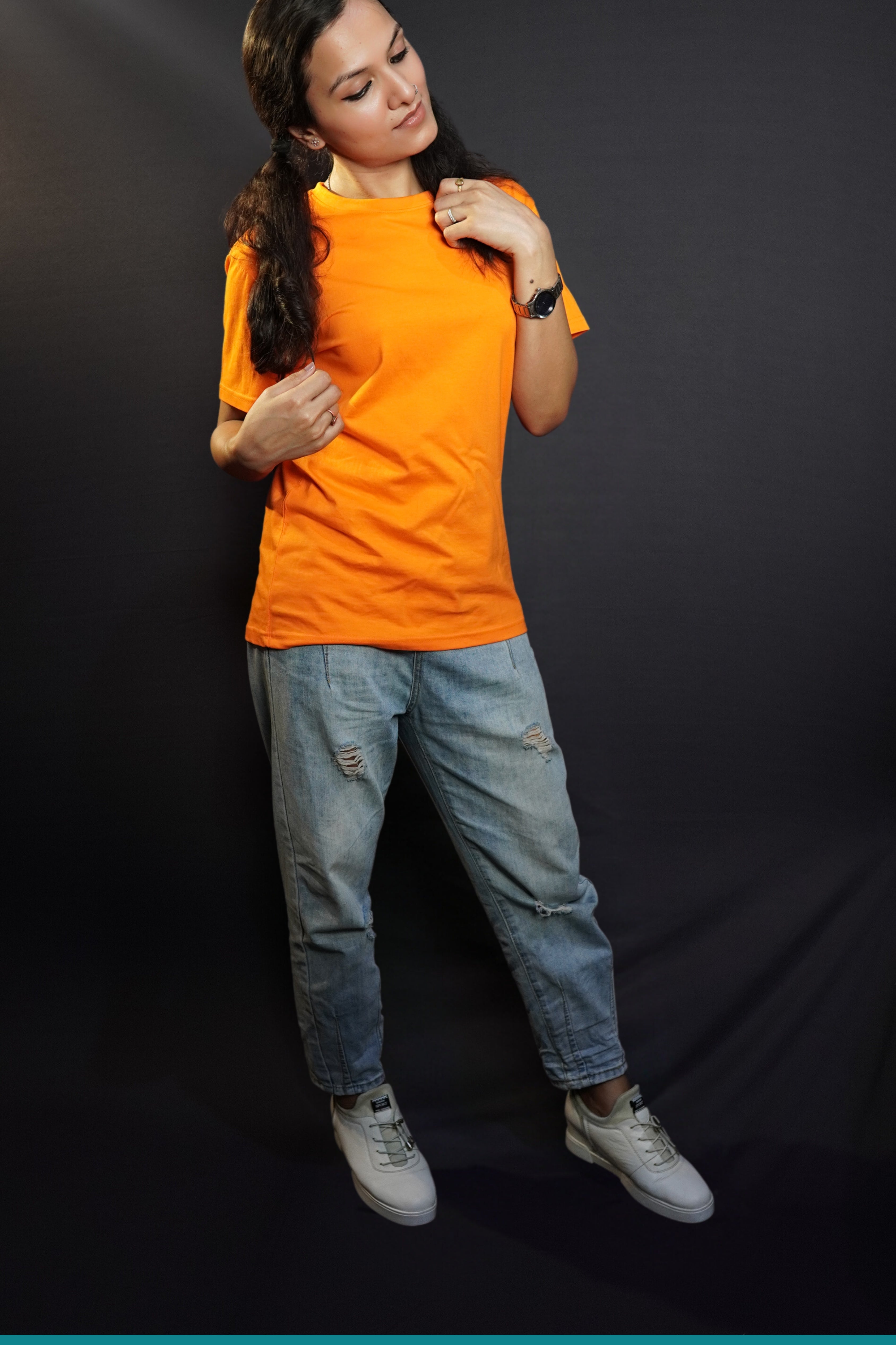 A model in a women's short sleeved summer tropical orange t-shirt, posing with hand grabbing a section of her short her and other just grabbing of the tip of other section on her shoulder, bending her head slightly, showcasing a modern informal look-Muselot