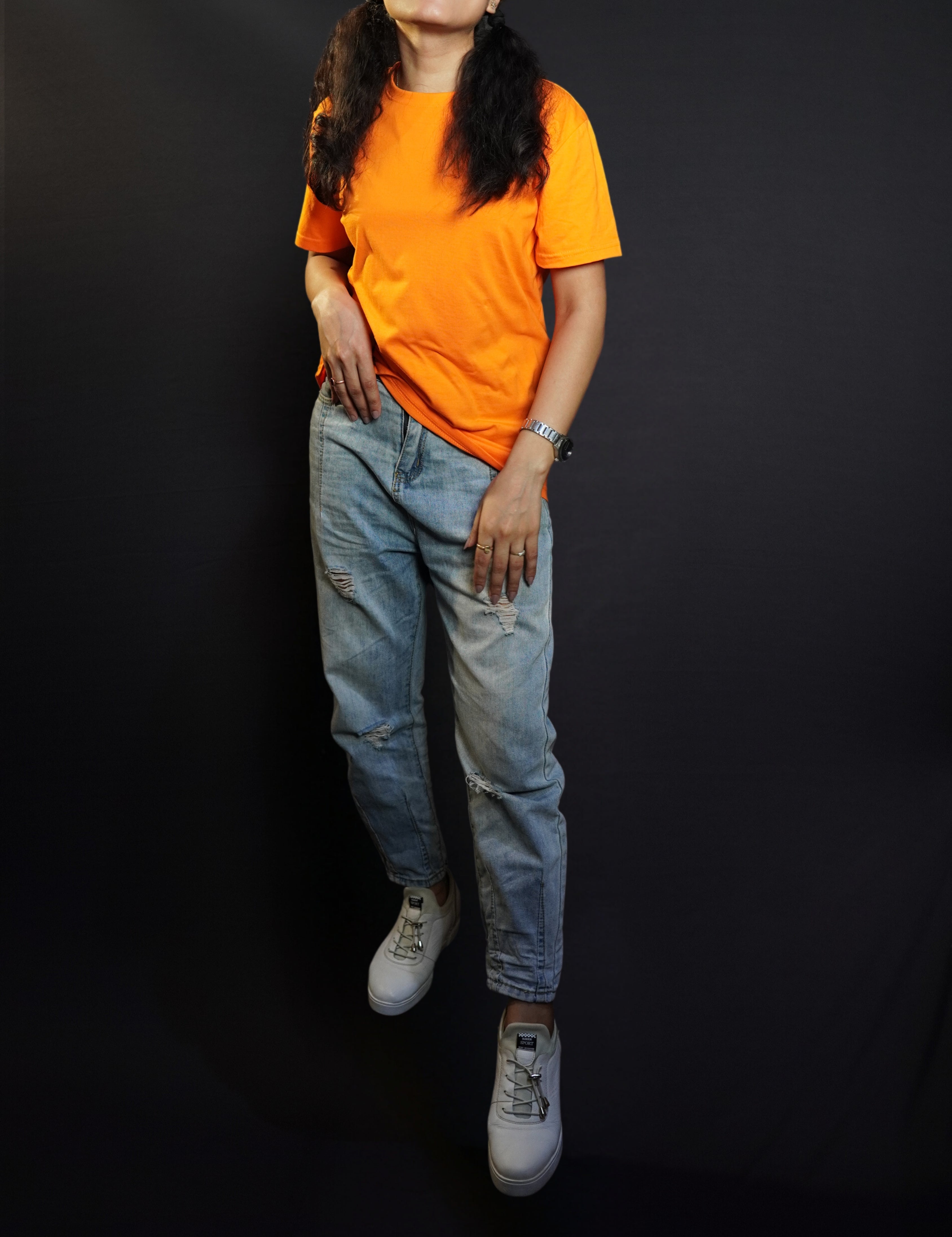 A stylish model posing happily as her hand is slightly inside her front pocket of her jeans, smiling happily, wearing a summer cotton plain tropical orange long length t-shirt, highlighting a cool modern look-Muselot
