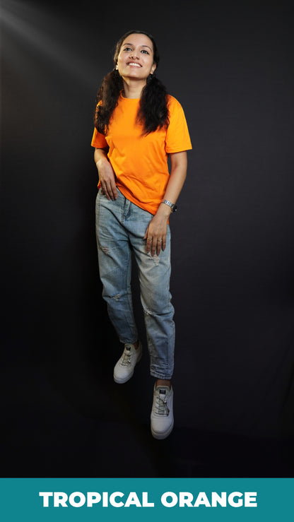 A stylish model posing happily as her hand is slightly inside her front pocket of her jeans, smiling happily, wearing a summer cotton plain tropical orange long length t-shirt, highlighting a cool modern look-Muselot