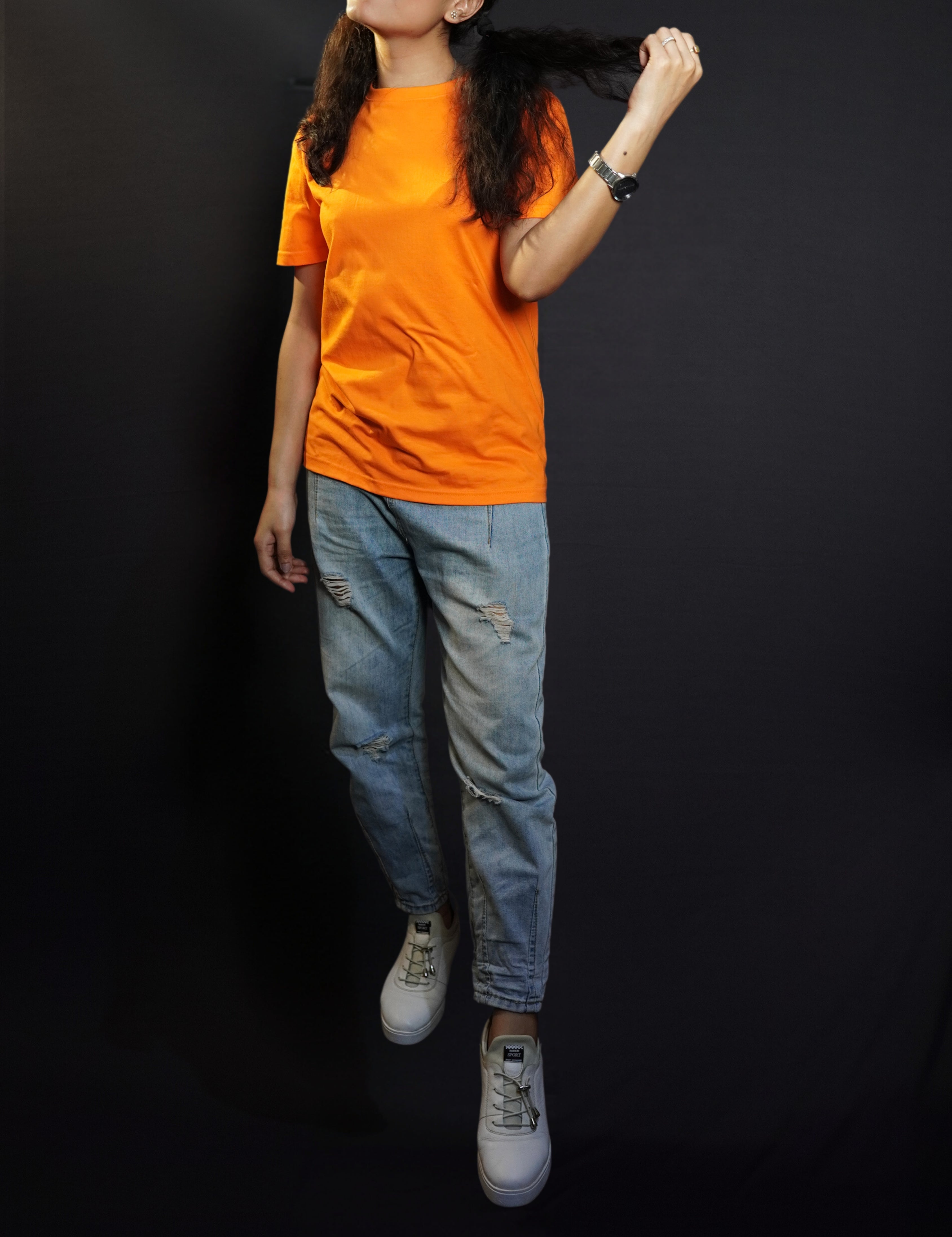 A woman wearing a long length short sleeved round neck plain cotton orange t-shirt, posing with her hand pulling a section of her short hair, showcasing a relaxed cozy fit-Muselot