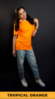 A woman wearing a plain round neck unisex tropical orange t-shirt, posing with her hand gently grazing her hair, smiling with her eyes, showcasing a stylish pretty look-Muselot