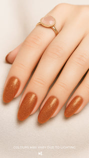 A shot of a model’s hand wearing Warm Gold Glitter nail stickies, showcasing the shimmering golden shade with a full glitter finish, highlighting the sparkle and festive charm of bold nail art in a smooth, salon-style look – Muselot.