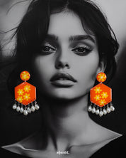 Model wearing the Zafraan floral earrings, featuring round orange studs with yellow flower motifs connected to hexagonal orange drops decorated with matching floral designs, finished with dangling white pearl-like beads, highlighting their vibrant and playful charm – Muselot.