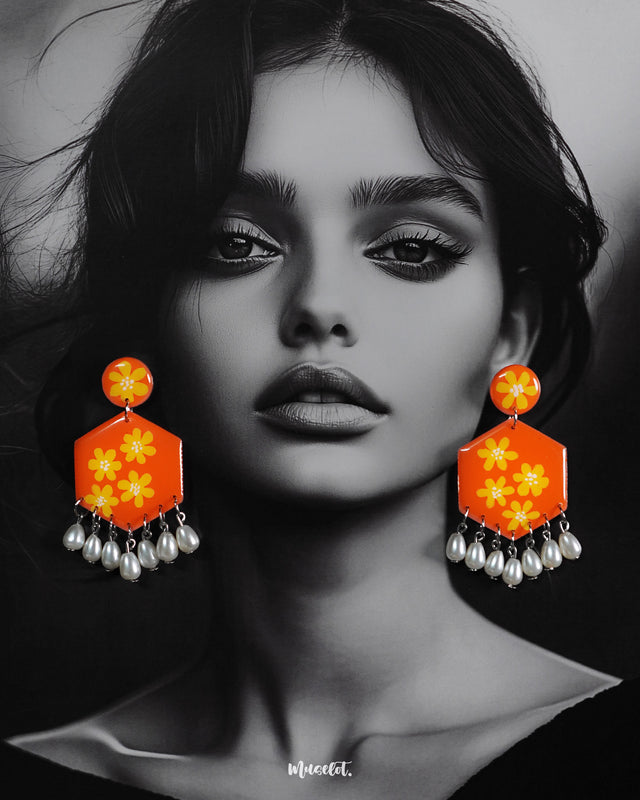 Model wearing the Zafraan floral earrings, featuring round orange studs with yellow flower motifs connected to hexagonal orange drops decorated with matching floral designs, finished with dangling white pearl-like beads, highlighting their vibrant and playful charm – Muselot.