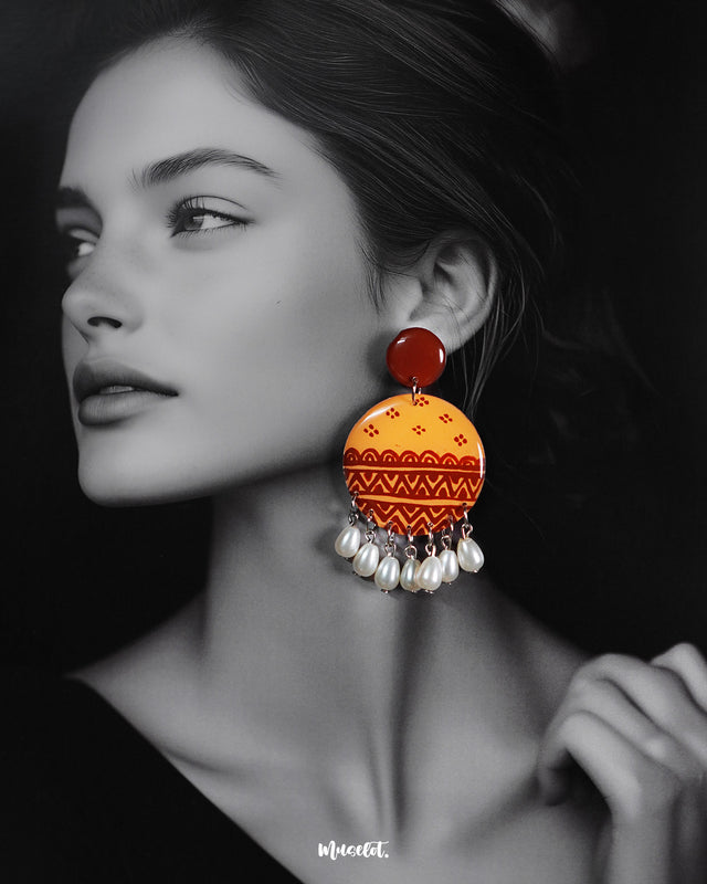 Model wearing the Zardozi drop earrings featuring hand-painted ethnic patterns in earthy tones of mustard and rust, accented with elegant white pearl drops—showcasing the graceful blend of traditional design and contemporary charm — Muselot.