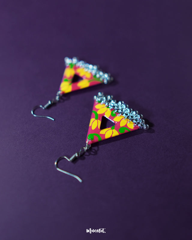 Triangle-shaped floral earrings with bright yellow and pink hand-painted flowers on a red base, highlighting their bold colors and showcasing dangling silver jhumki charms against a rich purple background — Muselot.