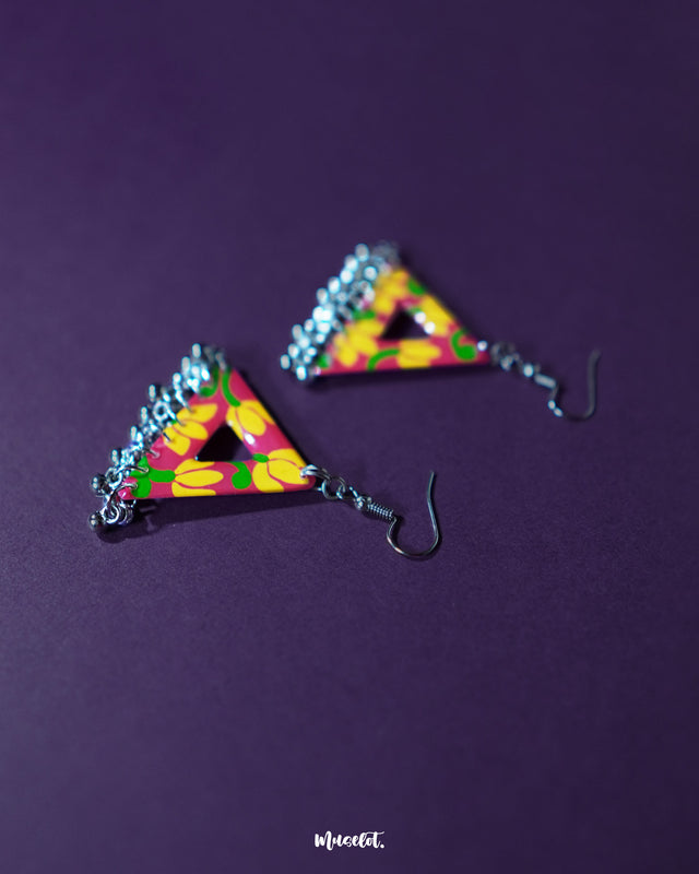 Zarmin triangle floral earrings rest against a rich purple background, highlighting the vivid yellow and pink hand-painted floral motifs and showcasing the playful silver jhumki drops that add movement and charm to the bold triangular silhouette — Muselot.