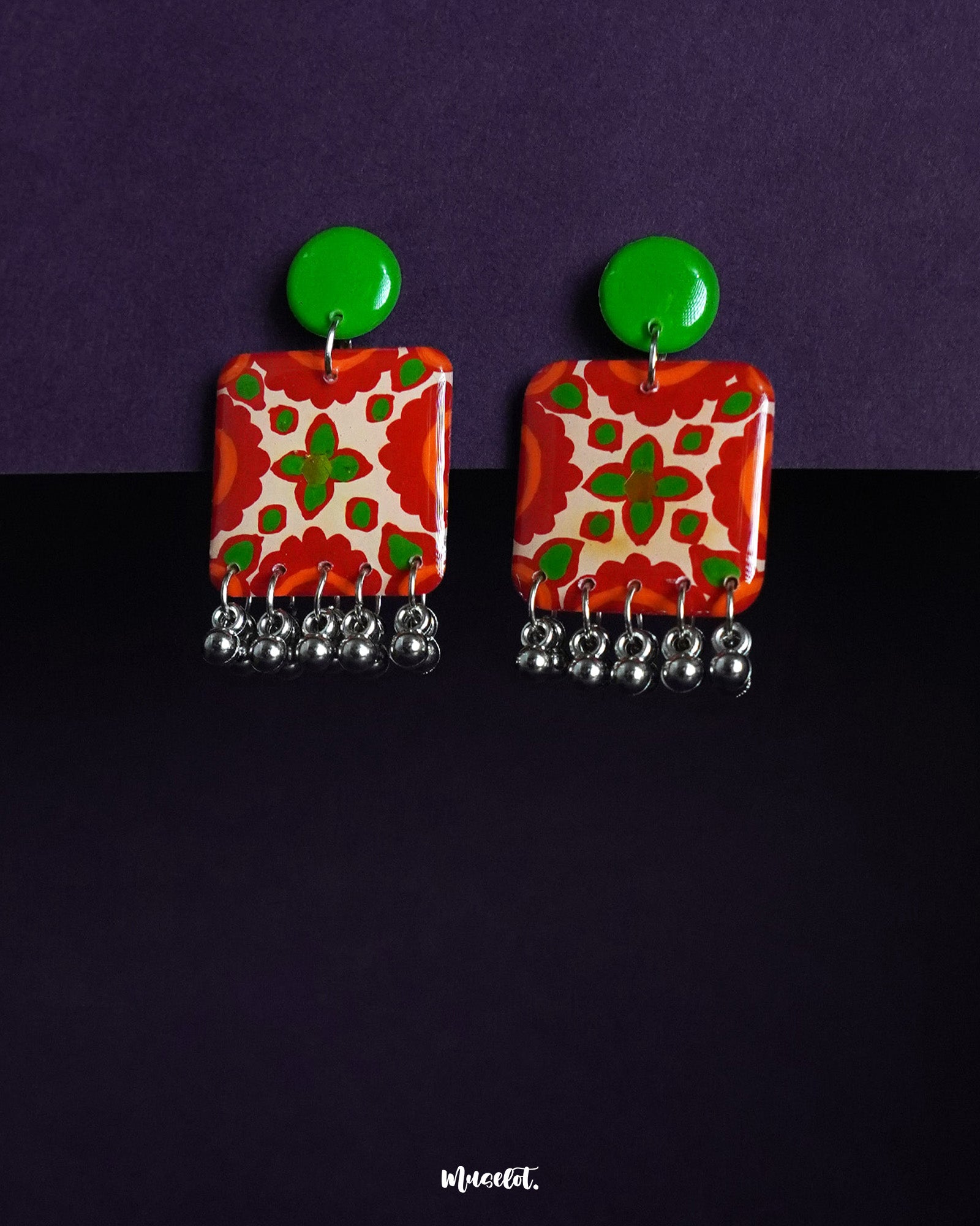 The Zarnigar stud earrings showcase vibrant red floral patterns with pops of green on a glossy square base, finished with metallic jhumki-style danglers for a festive, folk-inspired charm — Muselot.