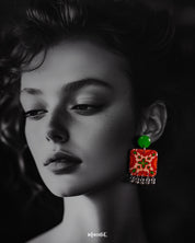A woman wears the Zarnigar stud earrings, their vivid red and green floral squares adding a bold burst of color near her face. The silver jhumki-style danglers catch the light, creating a playful contrast that enhances her look with handcrafted charm — Muselot.