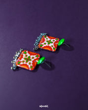 The Zarnigar stud earrings are showcased resting on a richly embroidered textile, their floral enamel work glowing in red, green, and ivory tones. The delicate silver ghungroos below add movement and a hint of melody, infusing the earrings with ethnic elegance — Muselot.