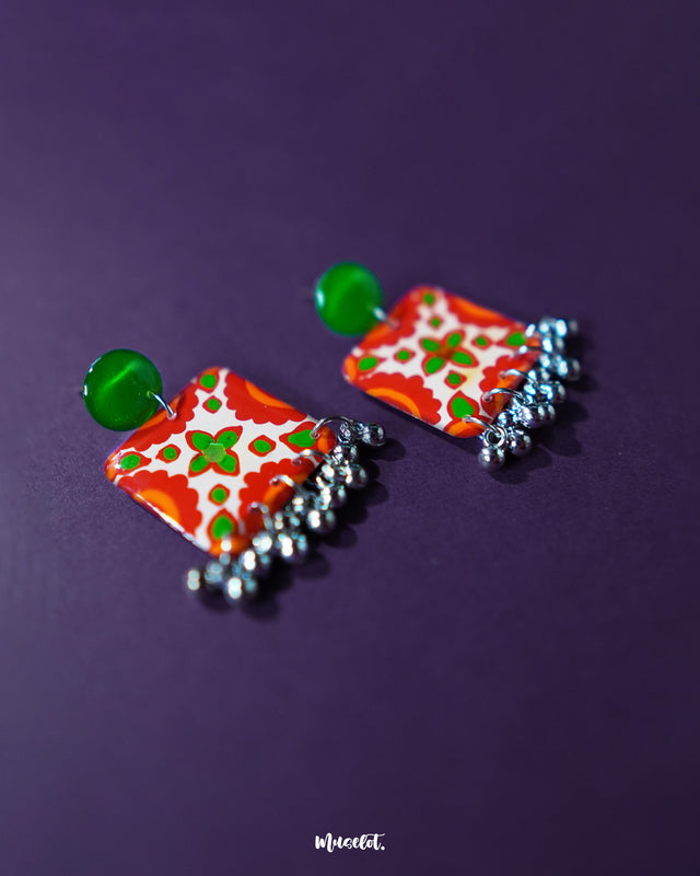 Zarnigar stud earrings displayed on a neutral base, showcasing their circular floral design with a rich blend of red, green, and gold hues. The tiny ghungroos add a playful touch, while the antique polish enhances the traditional handcrafted appeal — Muselot.