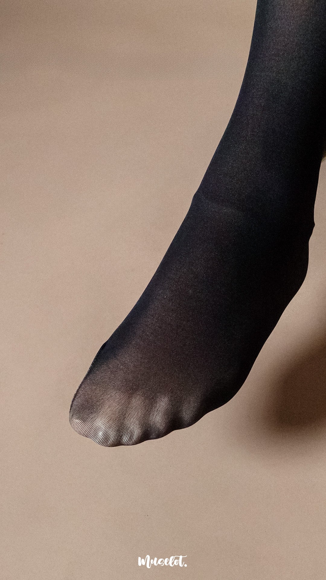 A model wearing black 50 denier sheer stockings on a neutral beige studio background, close-up of foot showcasing semi-opaque toe finish, fine knit texture and smooth natural leg appearance — Muselot