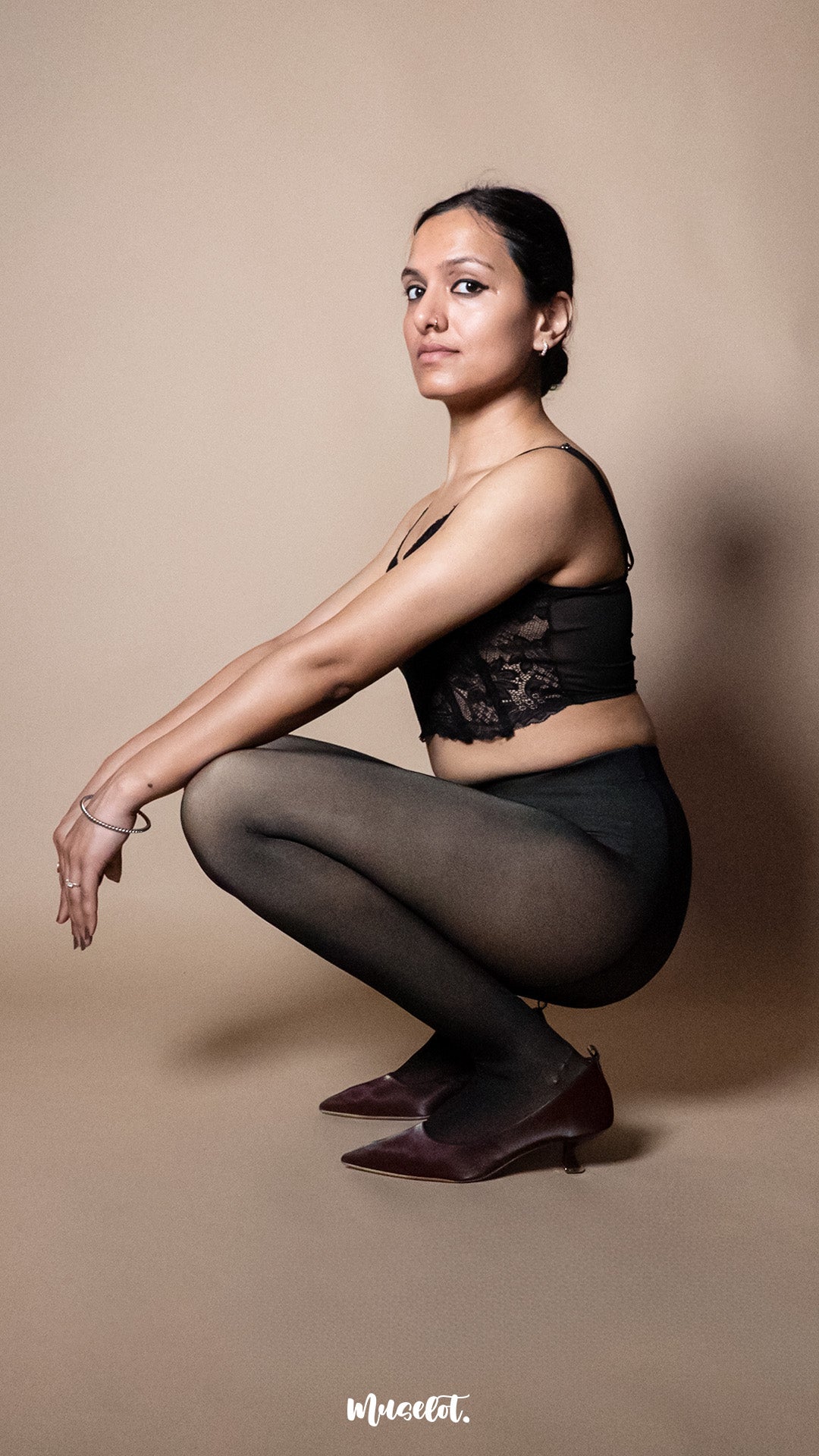 A model wearing black 50 denier stockings in squat pose on a beige backdrop, demonstrating stretch, flexibility and supportive high waist fit — Muselot