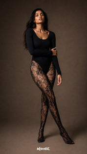 A woman standing with crossed legs in black semi-sheer fashion stockings featuring an all-over rose lace pattern and full closed-foot construction-Muselot