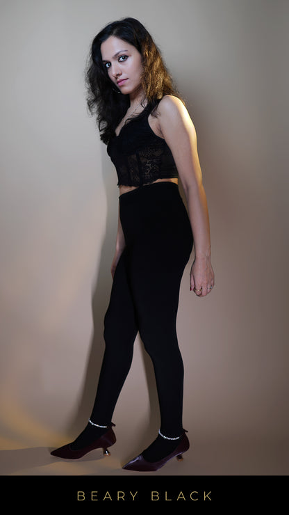 A model, wearing body-hugging warm black tights, is showcasing their sleek, form-fitting design that contours to the body while providing warmth and comfort. The deep black color highlights a stylish, versatile look, making these tights perfect for any occasion in cooler weather. -Muselot