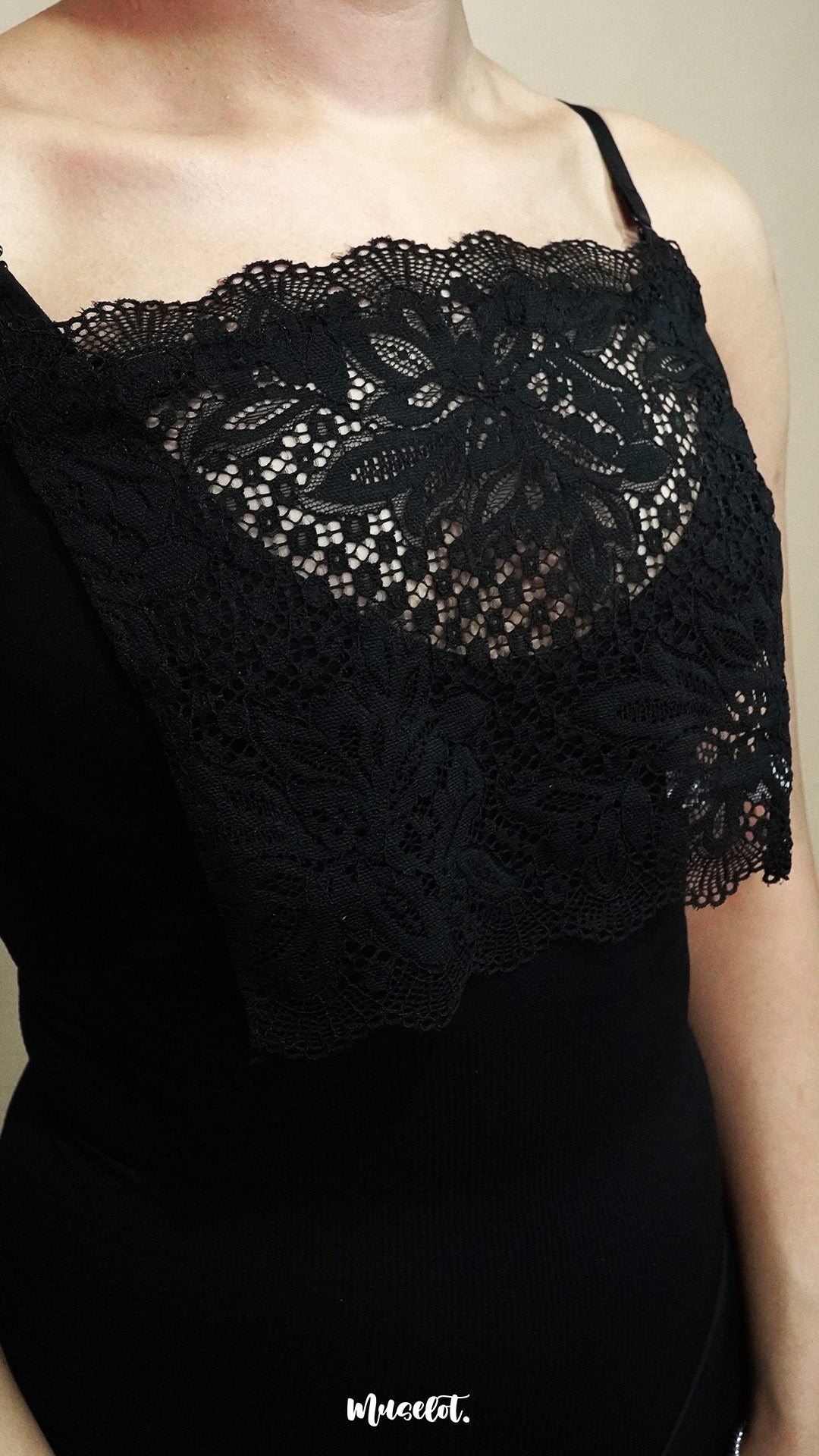 Close up of woman wearing black lace mock camisole over black top on beige background, showcasing wide lace panel that enhances neckline styling while keeping the look balanced – muselot
