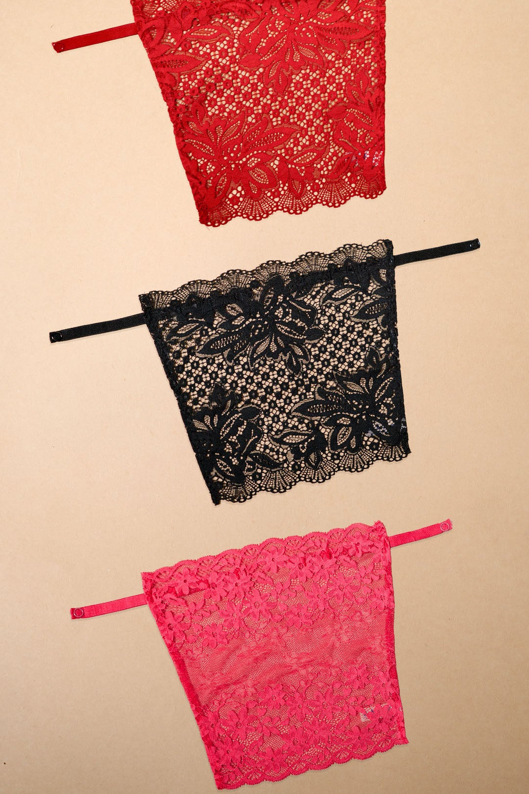 Three floral lace deep neck cover-up camisoles in red, black and dark pink displayed on a beige background, highlighting bold colour choices, delicate lace craftsmanship and stylish layering options for low-neck dresses, tops, blouses and partywear outfits – Muselot