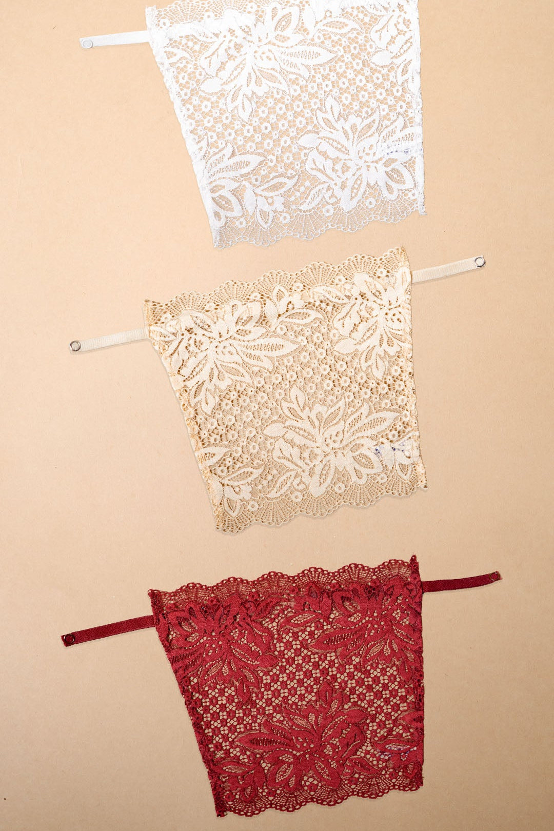 A set of clip-on lace camisoles for women displayed on a neutral beige background, featuring white, beige and maroon deep neck cover-up inserts with delicate floral lace detailing and adjustable straps for customizable neckline coverage — Muselot