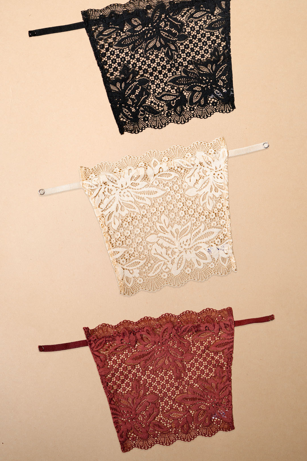 A pack of three clip-on neckline covers in black, beige and burgundy is displayed on a beige background. Featuring intricate floral lace, adjustable straps and elegant scalloped detailing, these deep neck cover-ups are designed to complement dresses, tops, kurtis and blouses. The lightweight clip-on camisole inserts provide stylish neckline coverage, effortless layering and a refined fashion accent, helping transform deep neck outfits into polished everyday and occasion-ready looks – Muselot