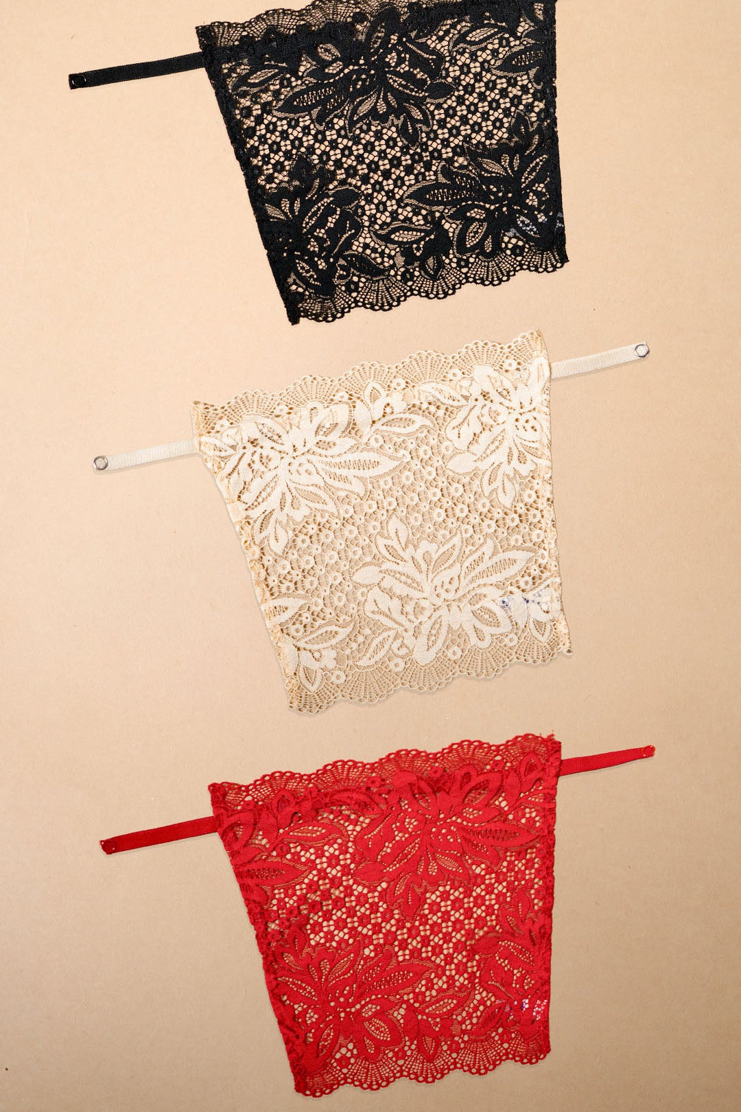 Three lace clip-on neckline covers in black, beige and red displayed on a beige background, showcasing intricate floral lace detailing, adjustable straps and versatile styling options. These deep neck cover-ups add elegant neckline coverage to dresses, blouses and low-cut tops while offering a lightweight, breathable alternative to traditional camisoles – Muselot