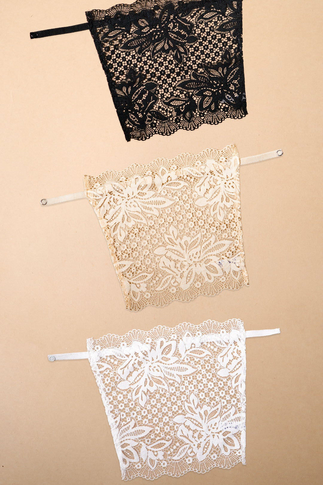 Three lace clip-on neckline covers in black, beige and white displayed on a beige background, featuring elegant floral lace patterns and adjustable straps. These deep neck cover-ups offer stylish neckline coverage for low-cut tops, dresses and blouses while adding a fashionable layered look without the bulk of a full camisole – Muselot