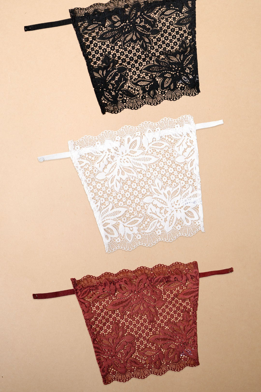 Three floral lace deep neck cover-up camisoles in black, white and burgundy displayed on a beige background, showcasing elegant colour combinations, intricate lace craftsmanship and versatile styling options for dresses, tops, blouses and low-neck outfits – Muselot