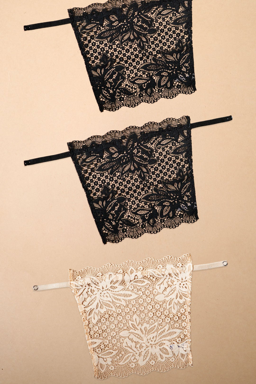 A pack of three clip-on neckline covers in black, black and beige is displayed on a beige background. Designed with rich floral lace, adjustable straps and delicate scalloped edges, these deep neck cover-ups help customise neckline coverage for dresses, tops, kurtis and blouses. The lightweight clip-on camisole inserts add elegance, confidence and layering versatility while blending naturally with different outfits for a polished everyday or occasion-ready look – Muselot