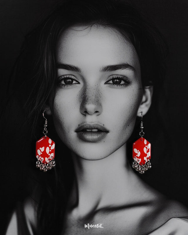 A model wearing the Mehar floral red hook earrings showcases the striking handcrafted design — vivid red hexagonal drops with delicate white floral motifs and metallic ghungroo accents, highlighting the bold contrast and showcasing a modern yet traditional fusion — Muselot.