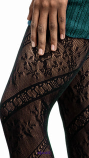 A model wearing black lace pantyhose with floral mesh design on a white background, close up shot highlighting pattern detail - Muselot