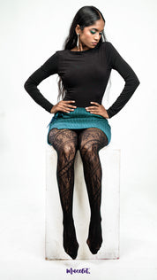 A model wearing black designer lace tights styled under a skirt on a white background, showcasing sheer patterned stockings - Muselot