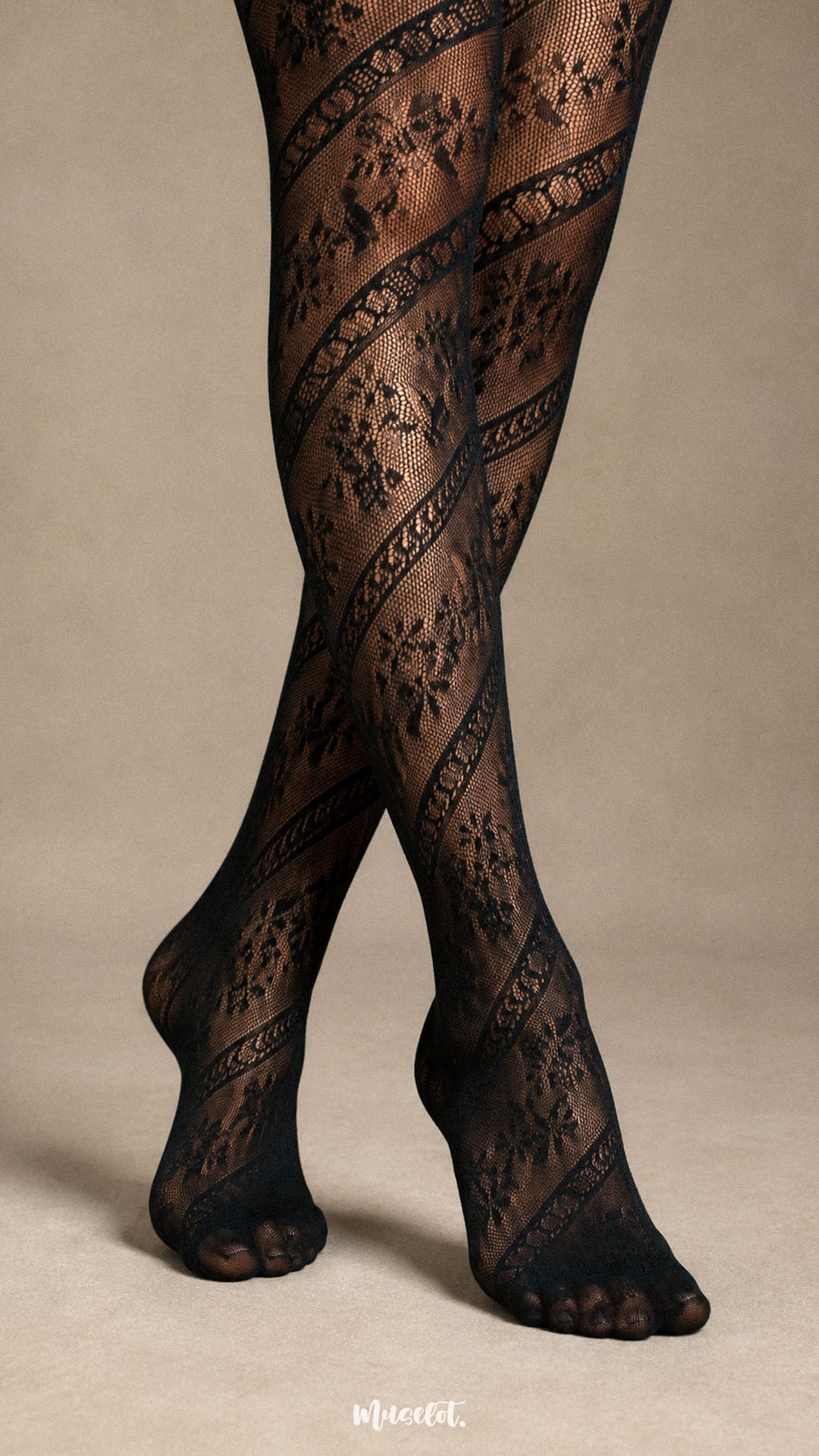 Close-up of crossed legs and feet in black lace pantyhose showing floral mesh motifs, diagonal lace bands and closed-toe construction - Muselot