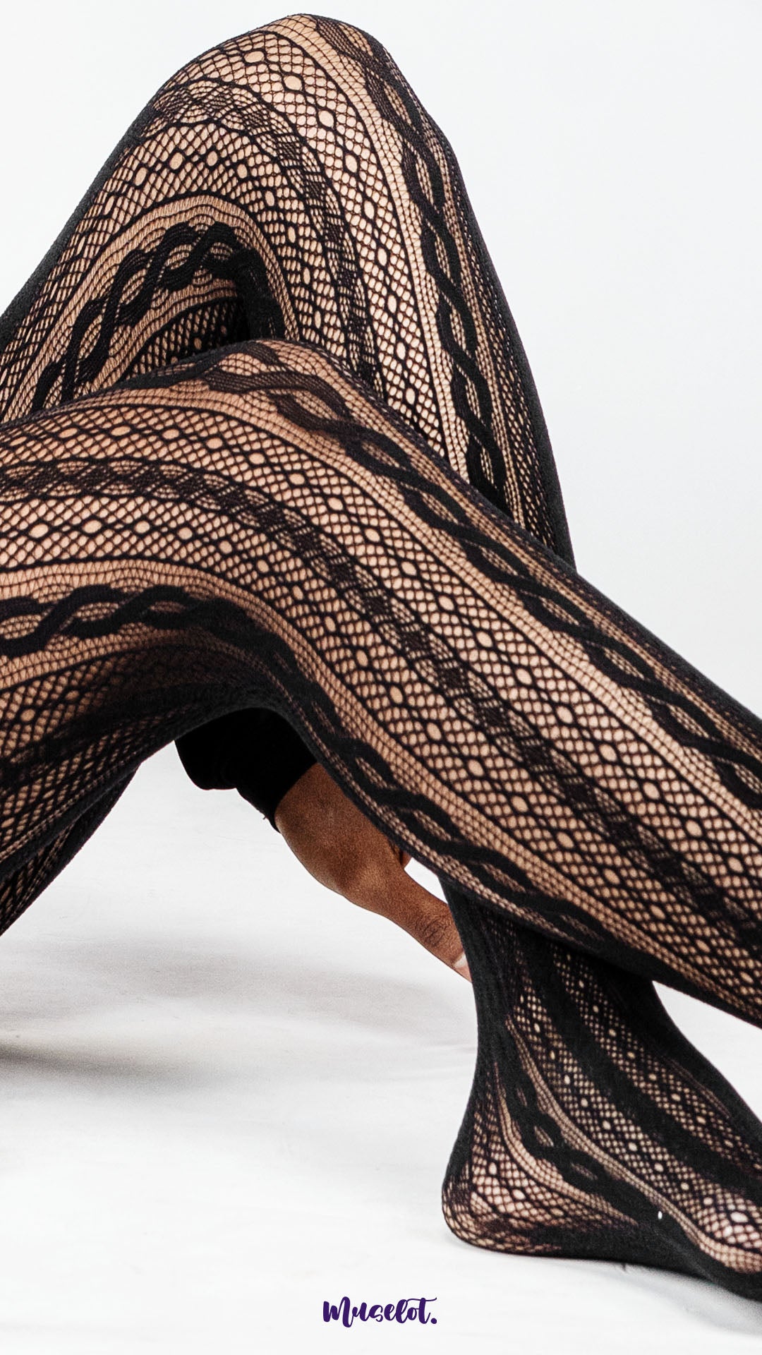 A close up of crossed legs wearing black patterned lace stockings on white background, highlighting intricate fishnet texture and net design for statement styling – Muselot