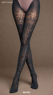 A focused view of crossed legs wearing Intense Grey lace stockings with ornate repeating motifs and fine semi-sheer texture - Muselot