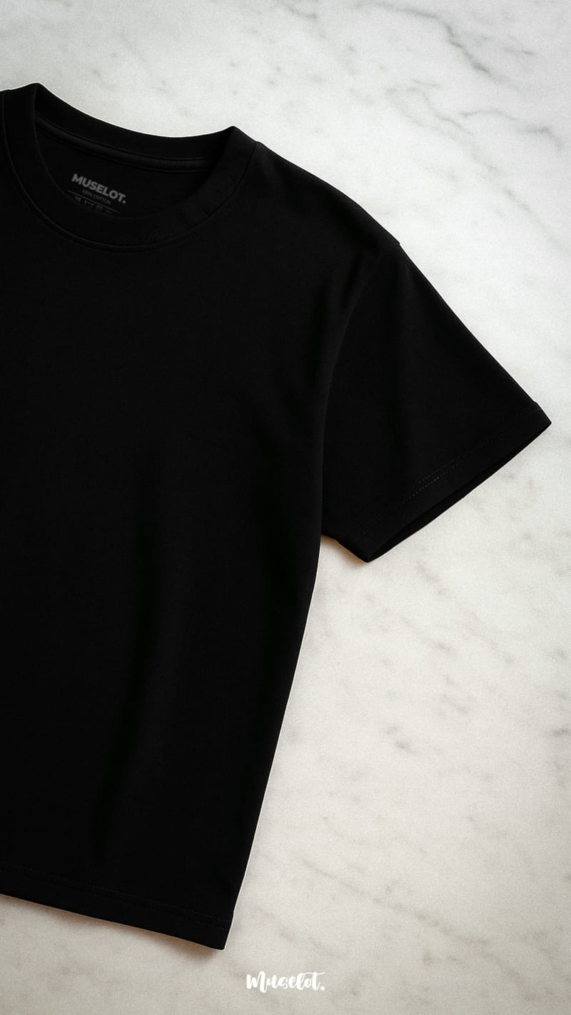 A half-flat lay shot of the unisex oversized black t-shirt placed on a sleek marble surface, showcasing its minimalist design and premium fabric—Muselot