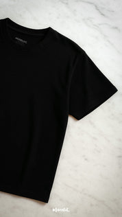 A half-flat lay shot of the unisex oversized black t-shirt placed on a sleek marble surface, showcasing its minimalist design and premium fabric—Muselot