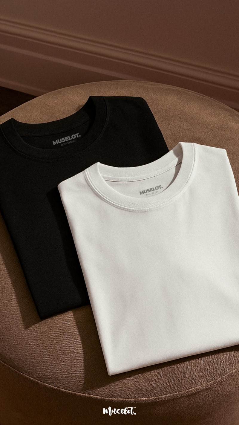 A flat lay shot of unisex oversized black and white t-shirt pair, kept neatly folded in a soft warm light highlighting the fabric’s texture and clean, minimalist design-Muselot