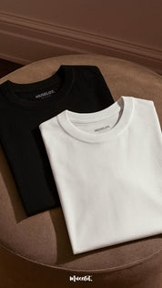 A flat lay shot of unisex oversized black and white t-shirt pair, kept neatly folded in a soft warm light highlighting the fabric’s texture and clean, minimalist design-Muselot