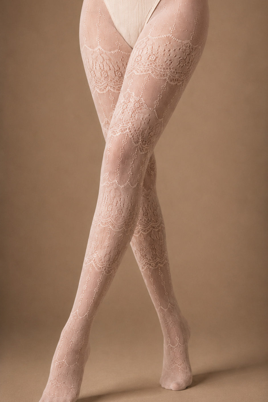 Close-up of crossed legs wearing pearl pink floral lace stockings, showcasing the repeating ornamental lace pattern from the thighs through the feet – Muselot.