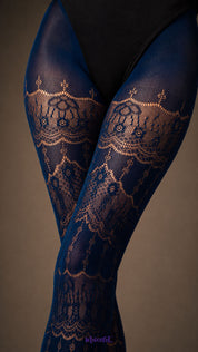 A close-up of Sapphire Blue designer lace pantyhose across the thighs showing intricate ornamental floral pattern and fine mesh texture - Muselot