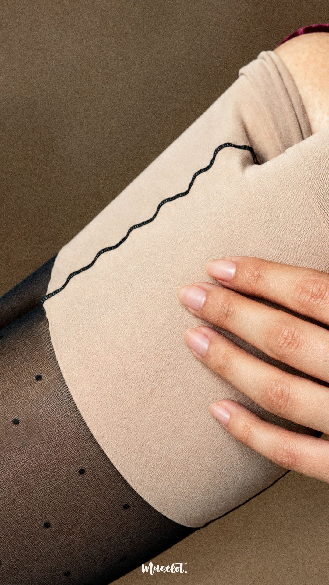 A close-up shot of a woman revealing the nude-toned inner layer beneath black sheer-effect polka dot stockings, showcasing the clever layered construction that creates a sheer appearance while offering added coverage - Muselot