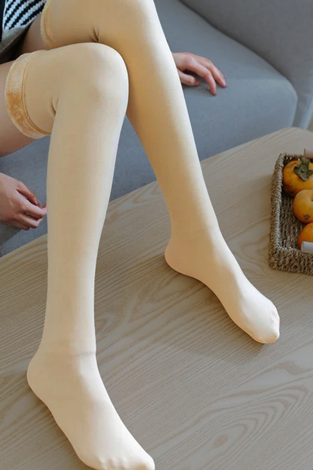 A woman wearing peachy skin-colored knee-high socks, sitting comfortably in a cozy interior with neutral-toned furniture. The socks, offering a soft and smooth texture, enhance her relaxed look while providing warmth and comfort, making them the perfect addition to any casual and cozy outfit-Muselot