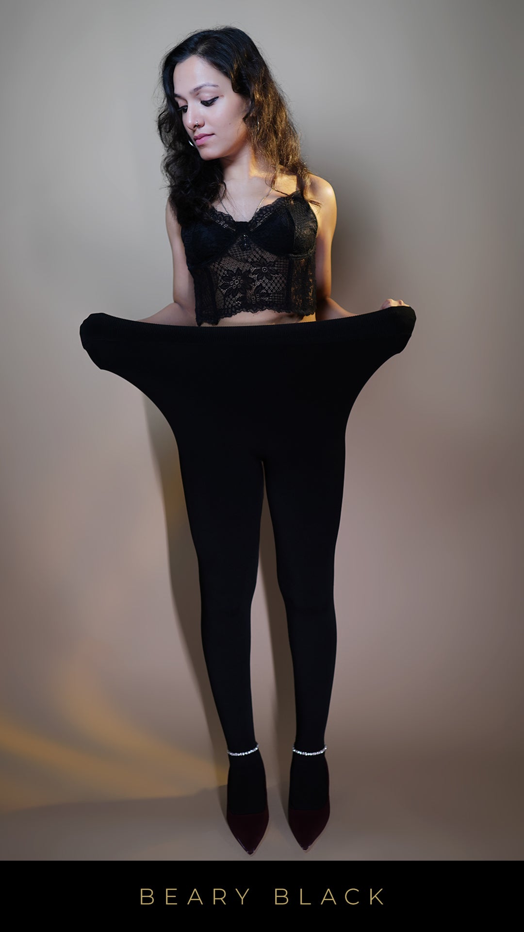 A model, stretching the waistband of black warm tight, to showcase its flexible, adjustable fit. The deep black color highlights a sleek, comfortable design, making these tights both cozy and versatile for everyday wear. -Muselot