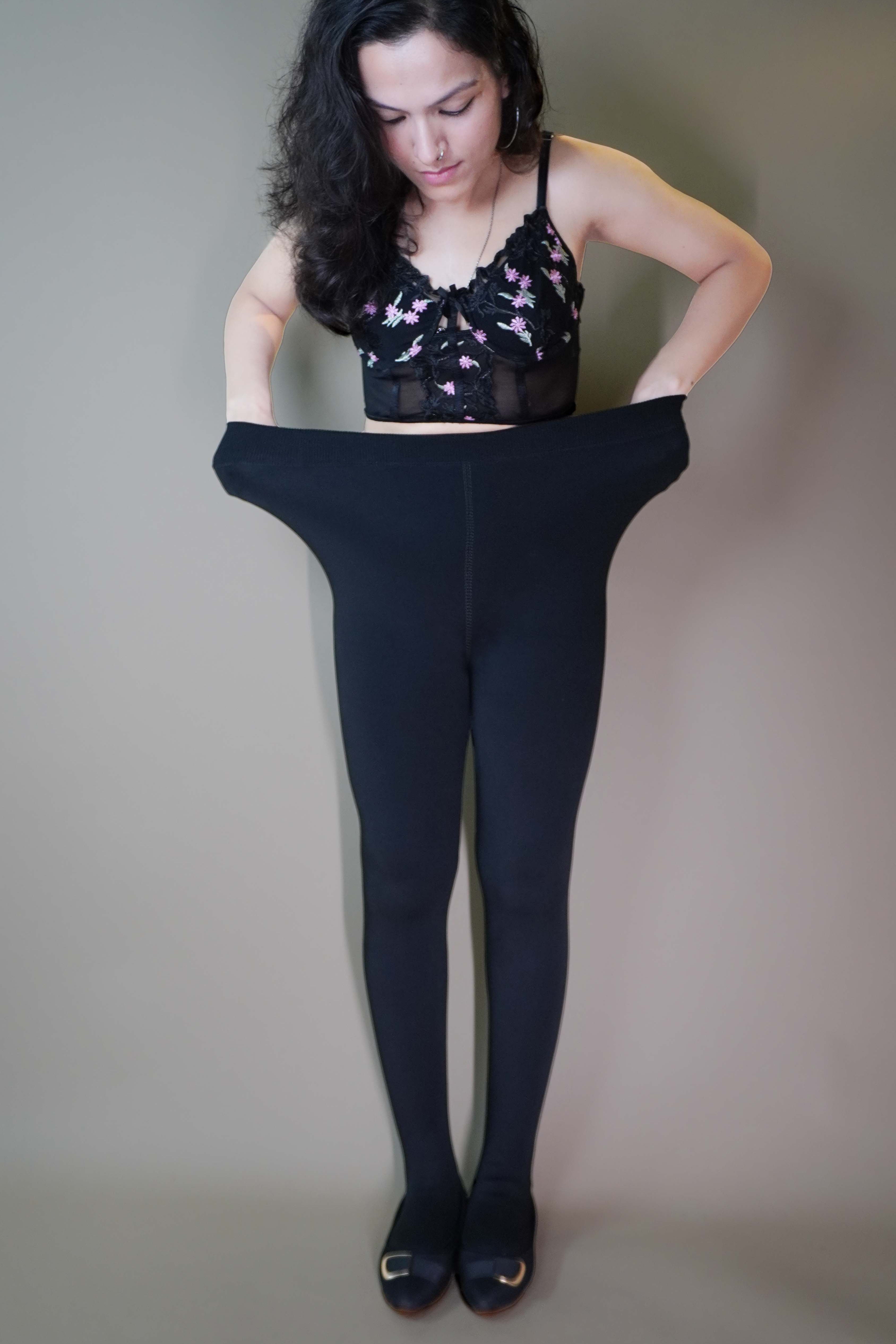 A model, wearing a fuzzy black warm tights, she is stretching the waistband to showcase their flexible and adjustable fit. The tights highlight their soft, fuzzy texture, providing both warmth and comfort while maintaining a sleek, form-fitting design. -Muselot