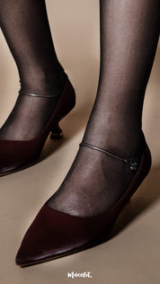 A model wearing black sheer pantyhose paired with pointed heels, close-up ankle shot on a beige background showcasing lightweight fabric and seamless foot coverage — Muselot