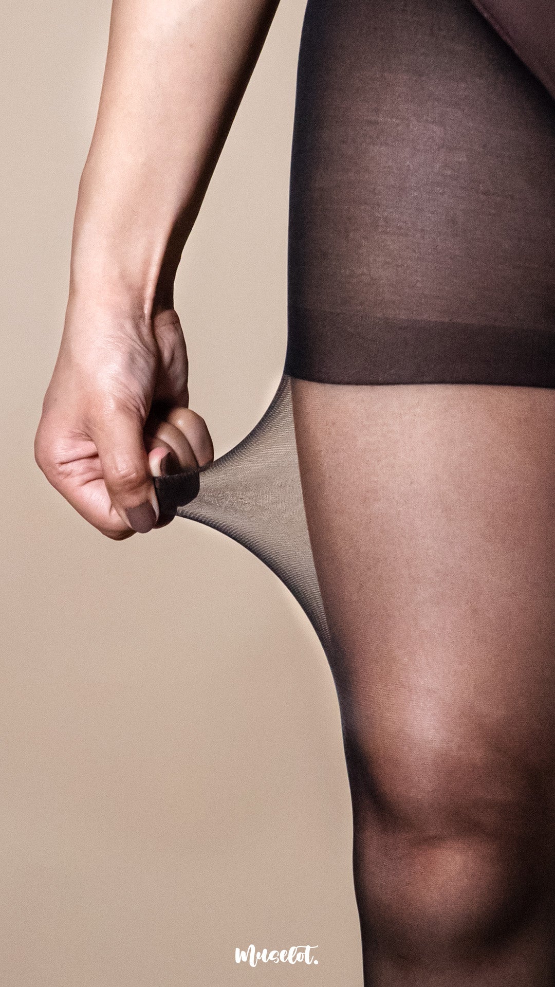 A model wearing ultra sheer black stockings, close-up thigh shot with hand stretching the fabric on a warm beige studio background, highlighting 15 denier transparency, high elasticity, and smooth second-skin finish — Muselot