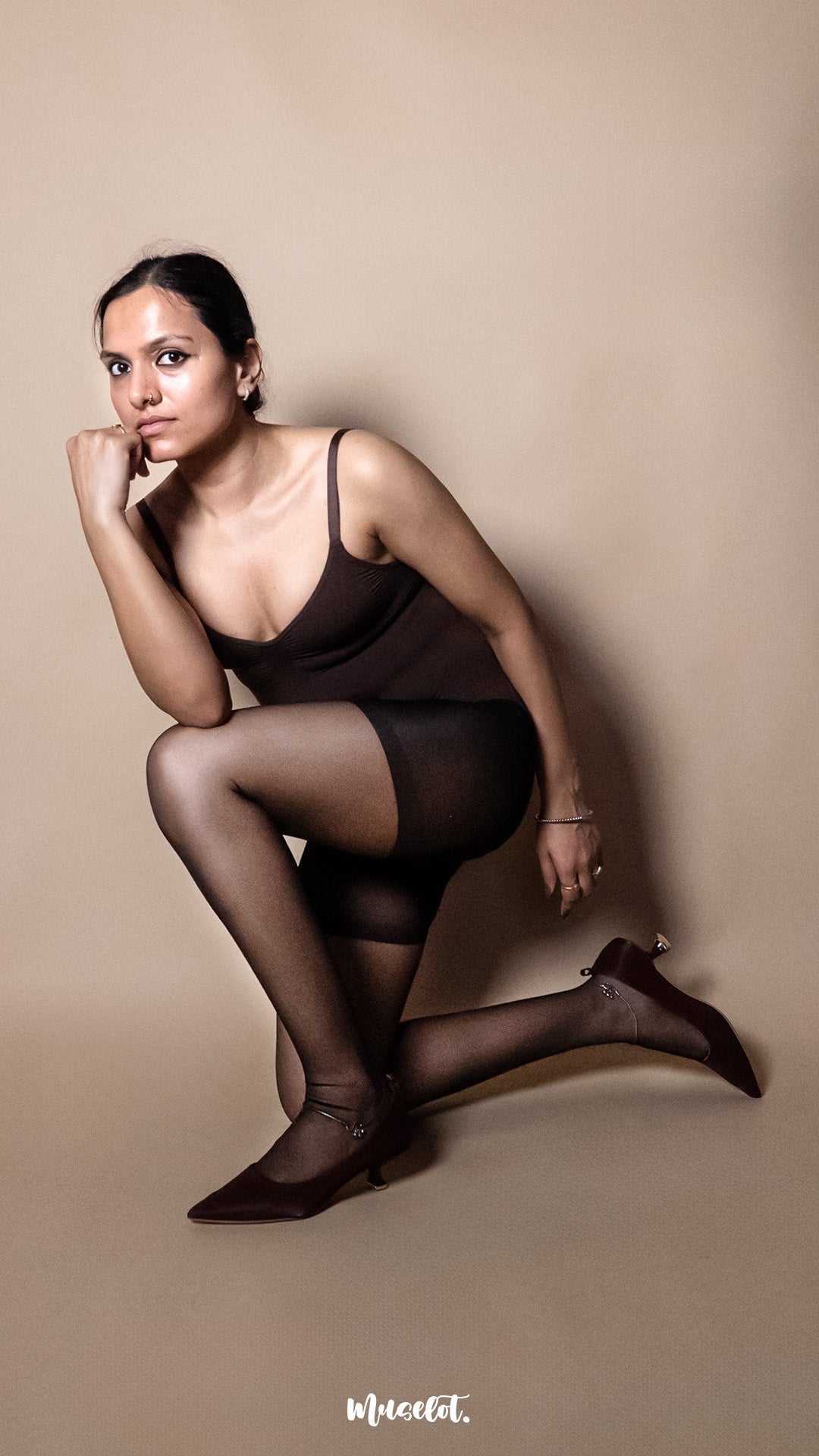 A model wearing black ultra sheer stockings styled with a bodysuit on a beige background demonstrating elasticity and tear-resistant fabric — Muselot